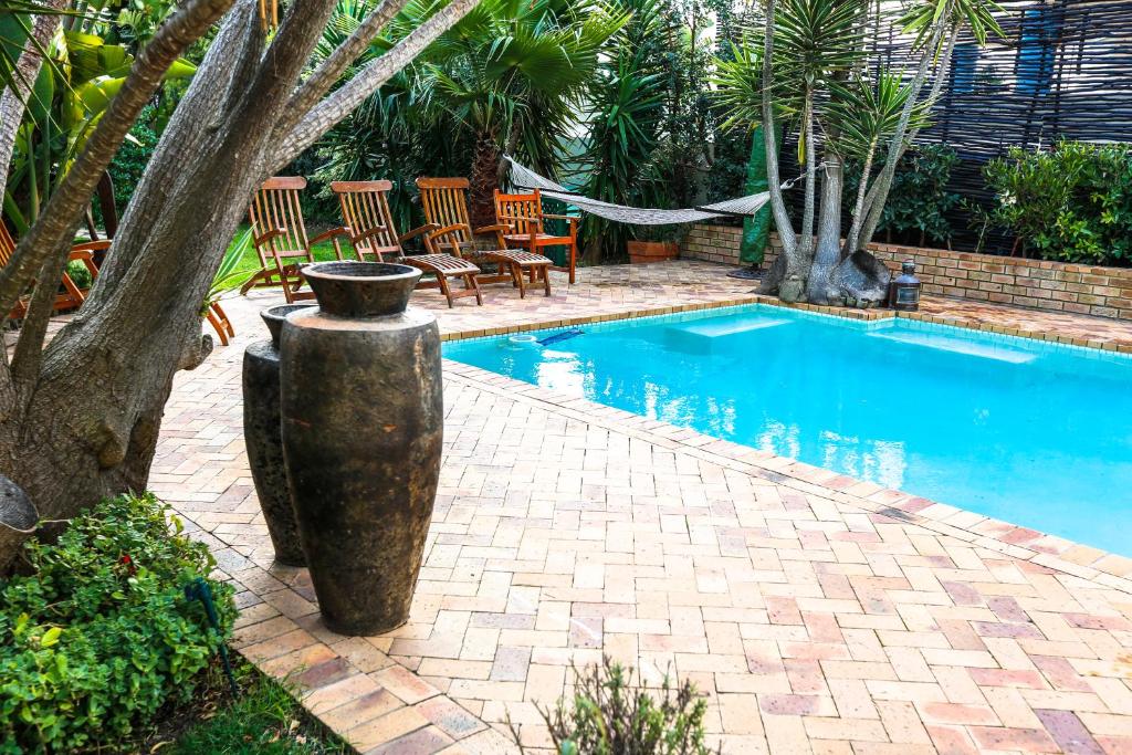 a swimming pool with a tree and chairs next to it at Secret Garden Guesthouse in Bloubergstrand