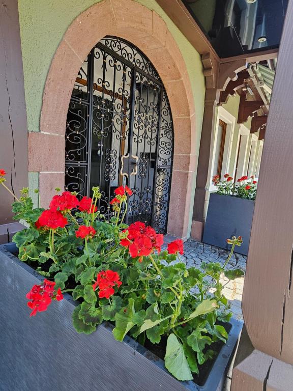 a black gate with red flowers in front of a building at L'Ecrin Vert & Spa in Kaysersberg