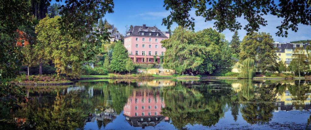 a building is reflected in the water of a lake at Hotel Goldner Anker in Bad Elster