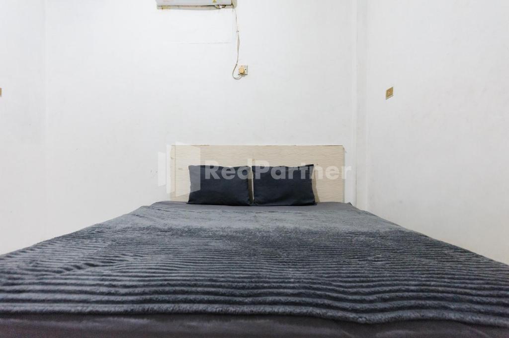 a bed in a white room with a pillow on it at Hotel Idayu Natuna Palembang RedPartner in Palembang