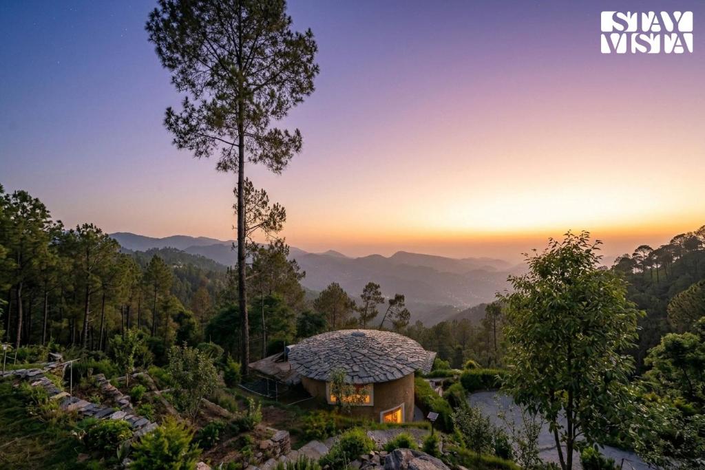 a house on a hill with the sunset in the background at StayVista at Sukoon Nature Retreat in Bhatrojkhan