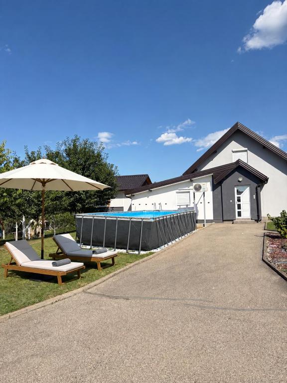 a building with a pool and an umbrella and two benches at Villa Eden Prijecani in Banja Luka