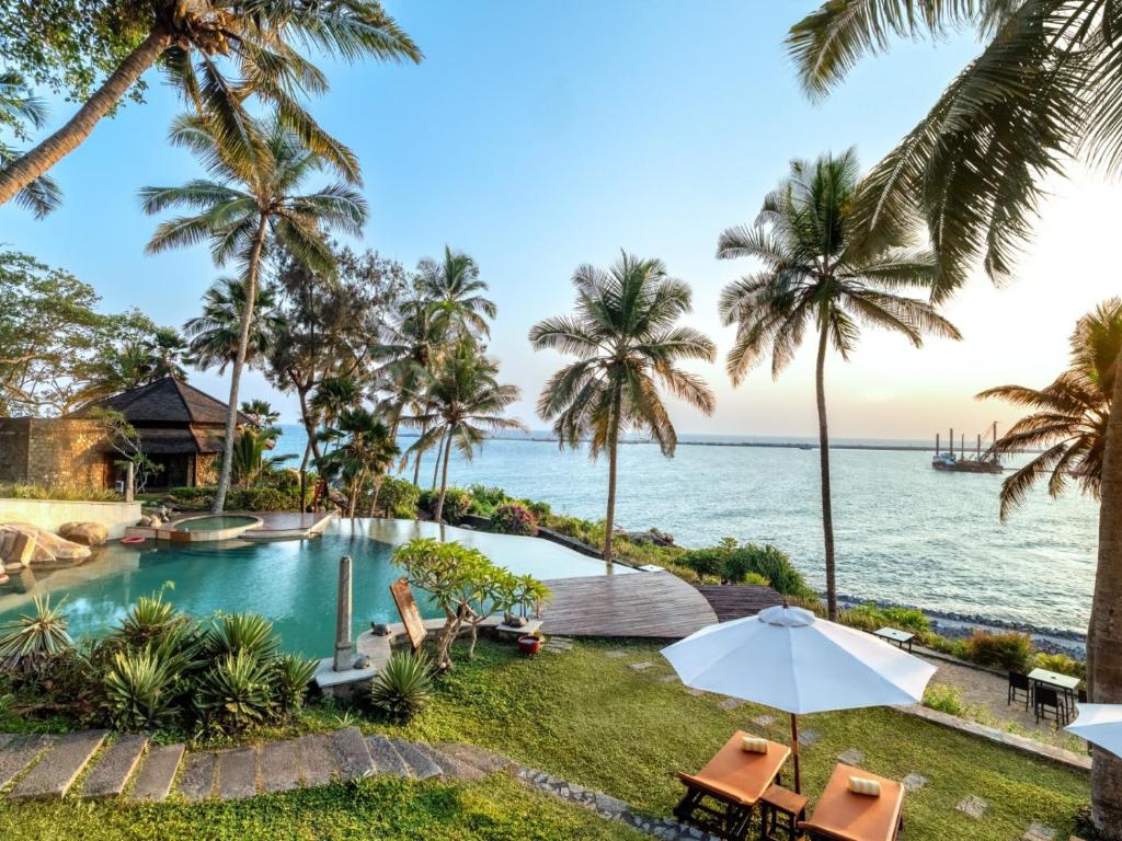 an infinity pool with palm trees and the ocean at Niraamaya Wellness Retreats, Surya Samudra, Kovalam in Kovalam