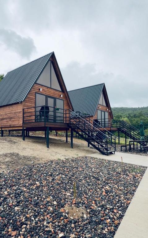 two large wooden huts with large windows and a gravel area at რაჭული სიმშვიდე Racha Serenity in Nikortsminda