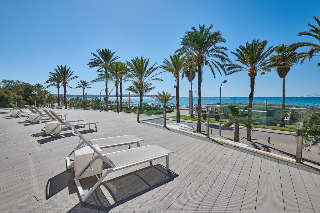 a row of lounge chairs and palm trees next to the beach at Grupotel Acapulco Playa - Adults Only in Playa de Palma