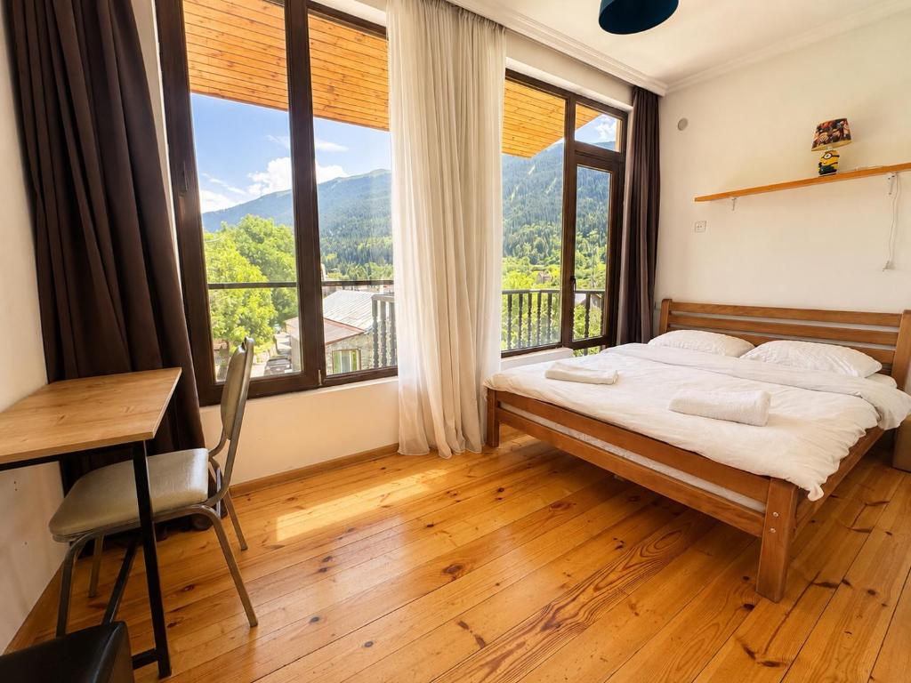 a bedroom with a bed and a desk and large windows at Eka's guest house in Mestia