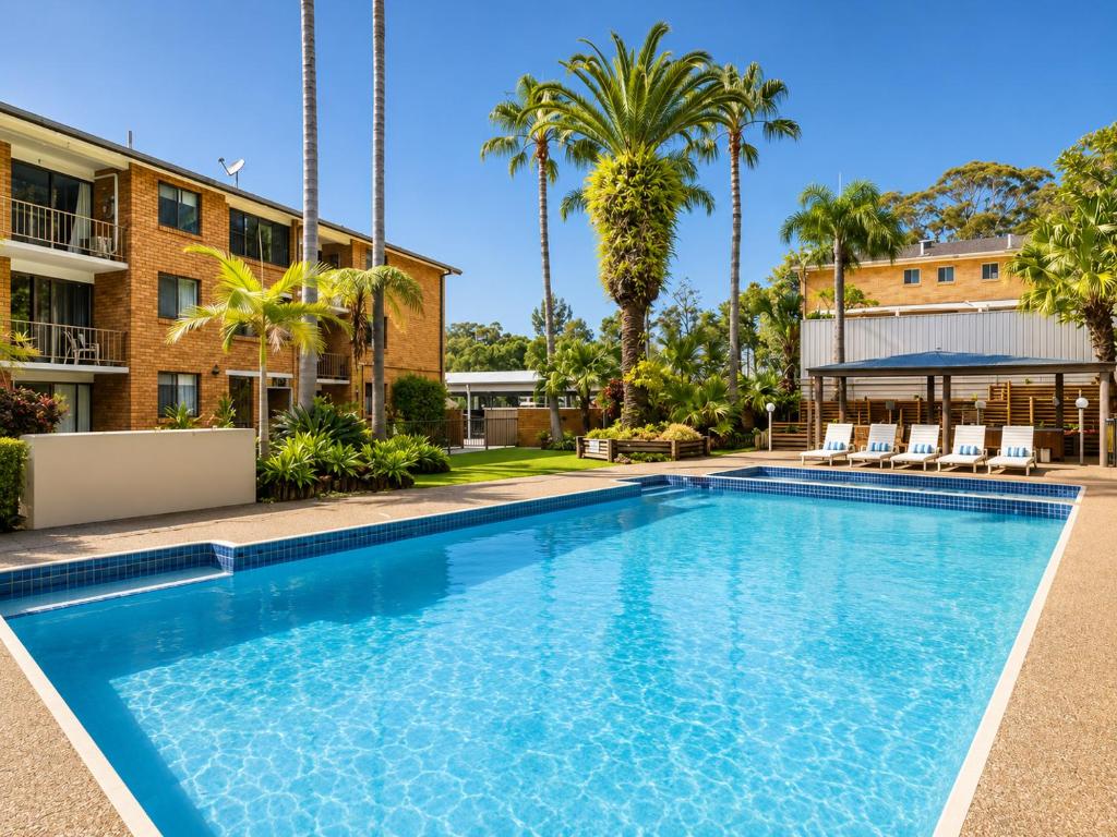 a swimming pool in front of a building with palm trees at Dunes Apartment Unit 8- GROUND FLOOR WITH POOL VIEW in Coffs Harbour