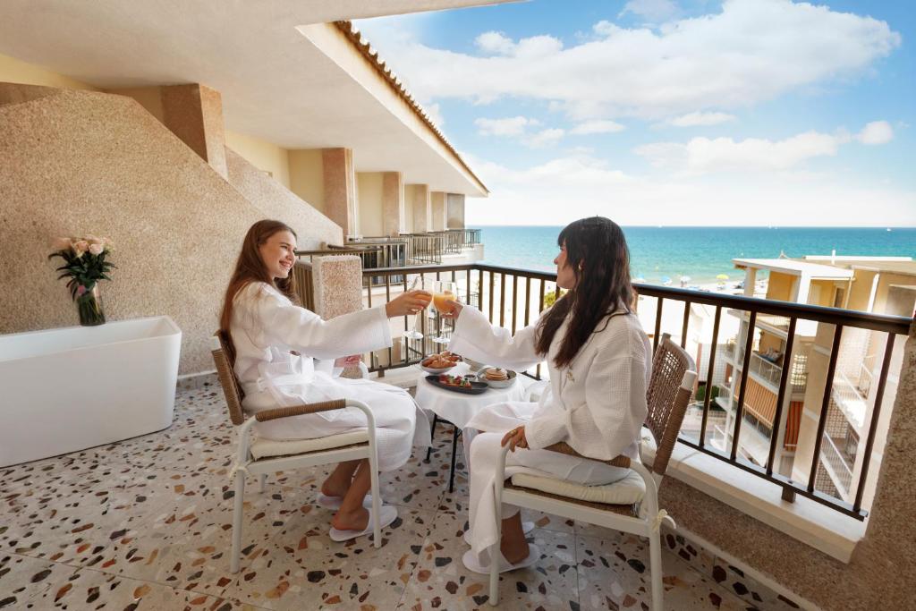 Zwei Frauen sitzen an einem Tisch auf einem Balkon mit Blick aufs Meer in der Unterkunft Hotel Guardamar in Guardamar del Segura