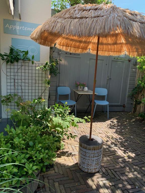 a straw umbrella in a patio with two chairs and a table at Appartement 't Loft in Zandvoort