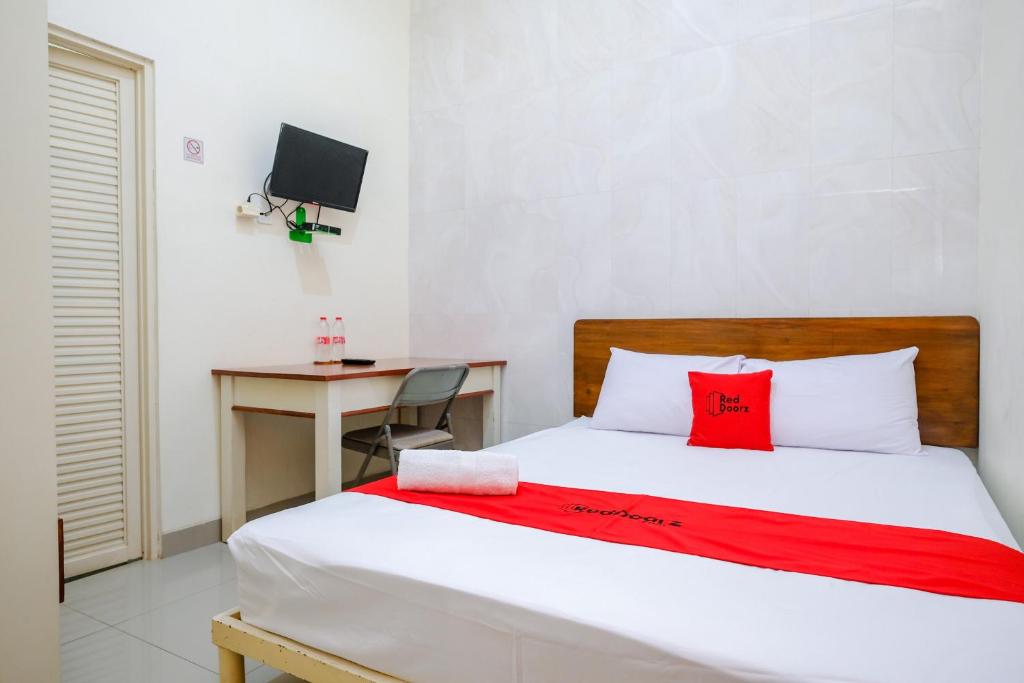 a bedroom with a bed with a red blanket and a desk at RedDoorz at Syariah House Purwokerto in Purwokerto