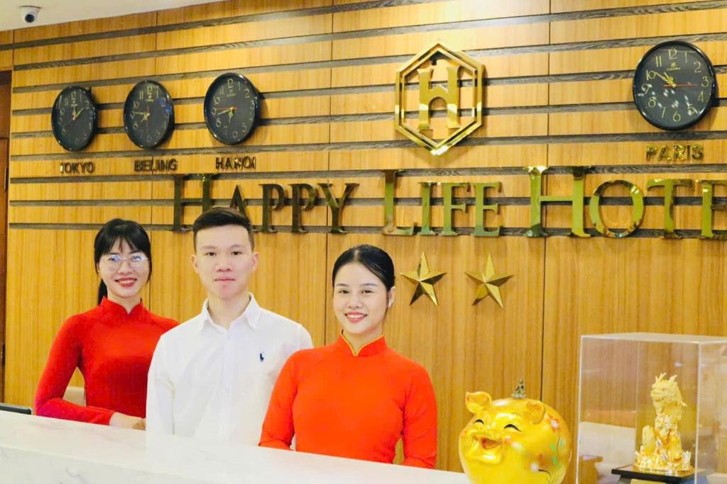 three people standing behind a counter with clocks on a wall at Happy Life Hotel District 7 Gần SECC in Ho Chi Minh City