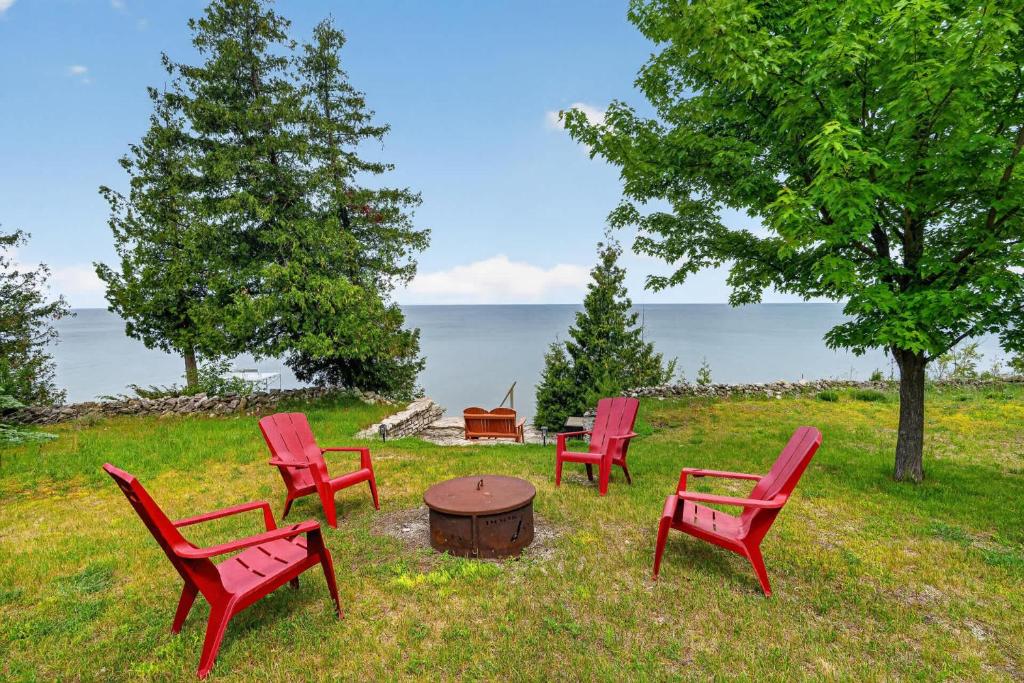 a group of red chairs and a table in the grass at Egg Harbor Waterfront home in Egg Harbor