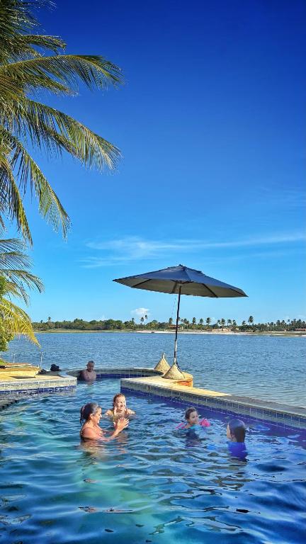 a group of people in a swimming pool with an umbrella at Xodó da Lagoa in Beberibe