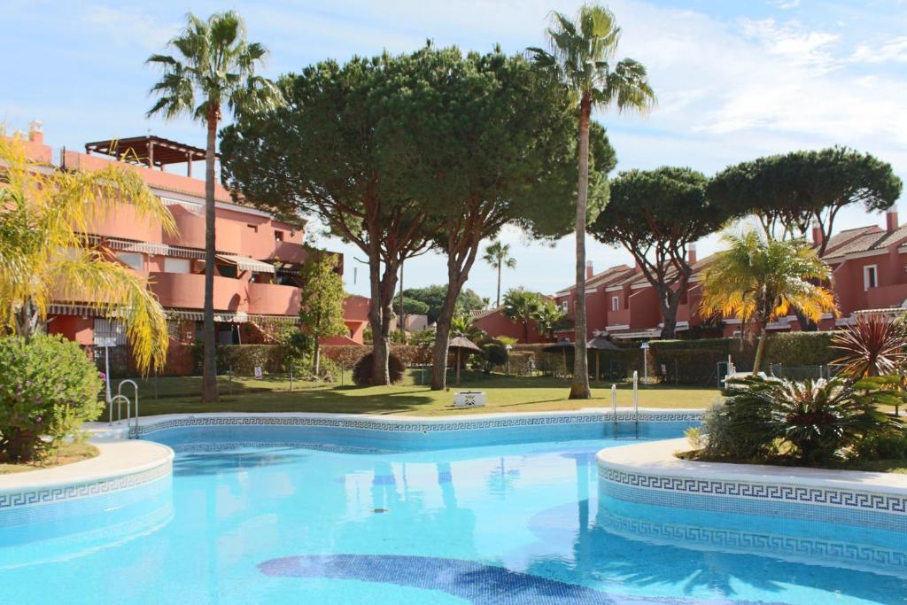 a large swimming pool with palm trees and buildings at Apartamento Pink Mariposas in Chiclana de la Frontera
