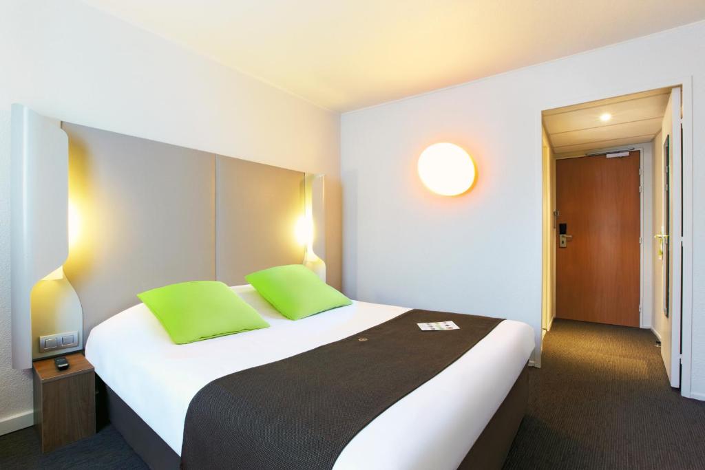 ein Hotelzimmer mit einem großen Bett mit grünen Kissen in der Unterkunft Campanile Saint-Quentin-En-Yvelines in Montigny-le-Bretonneux