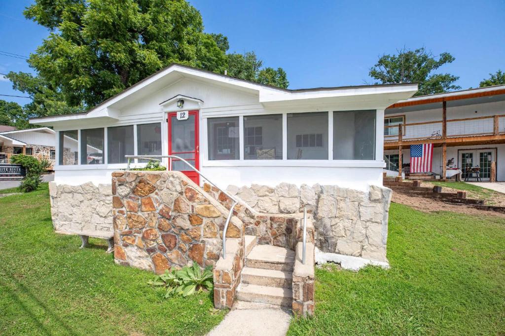 a white house with a stone wall and a red door at Historic Rockaway Beach Cottage 12 in Rockaway Beach