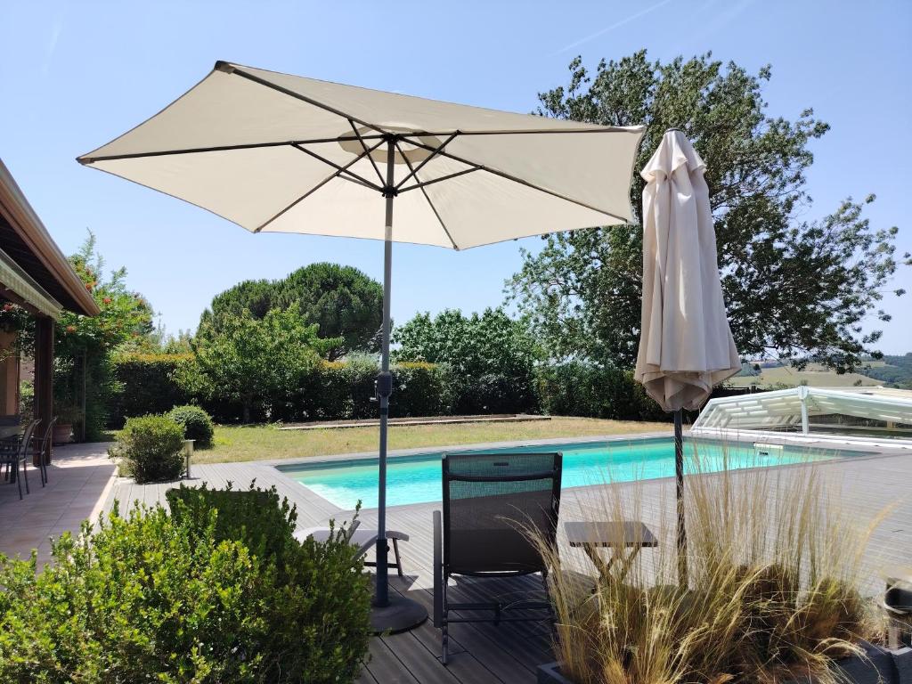 a white umbrella and chairs next to a swimming pool at Maison d'hôtes Beauregard in Donneville