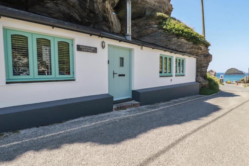 a house with green windows and a stone wall at Smugglers Cottage in Tintagel
