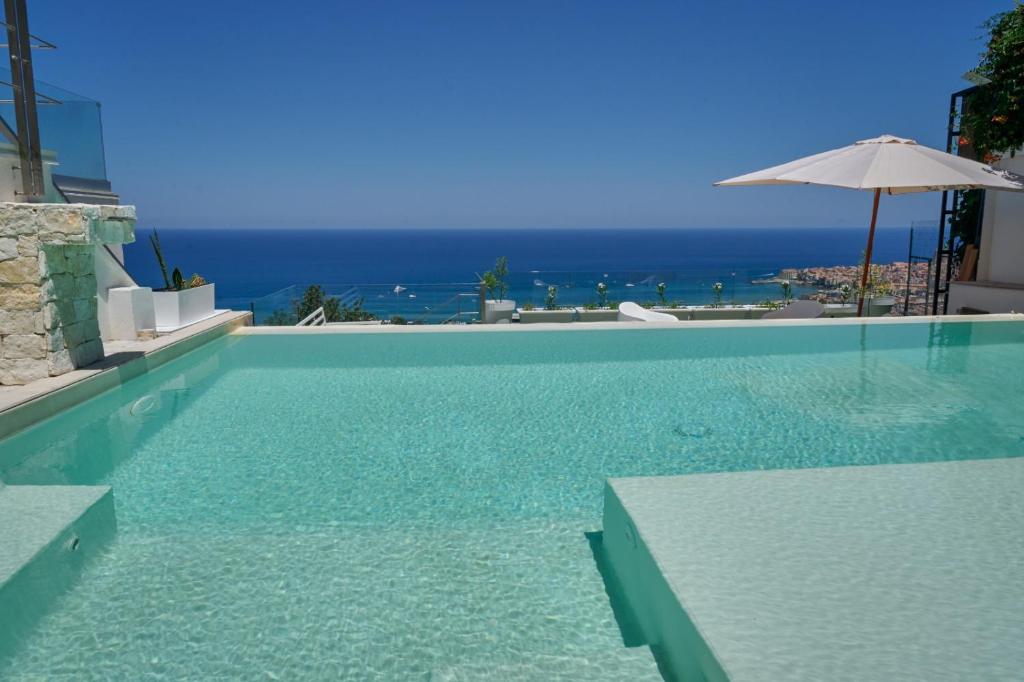 a swimming pool with an umbrella and the ocean at Villa AmOr in Cefalù