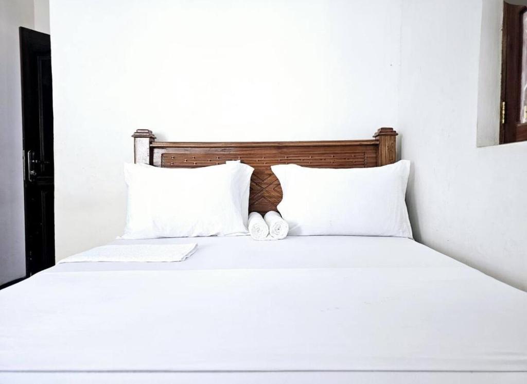 a bed with white sheets and two white pillows at Hello Rafiki Hotel Stone town in Ngambo
