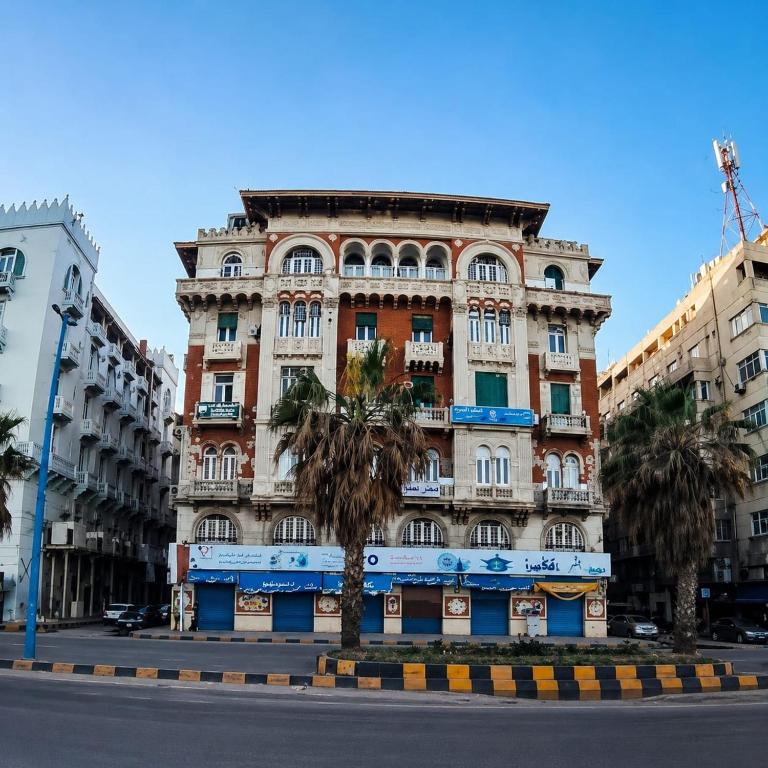 a tall building with palm trees in front of it at New Welcome House Hotel in Alexandria