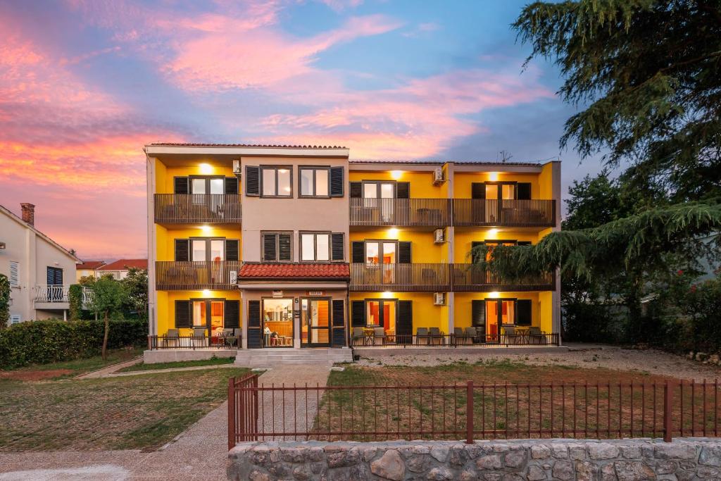 a large yellow building with a sunset in the background at Maja Apartments Malinska in Malinska
