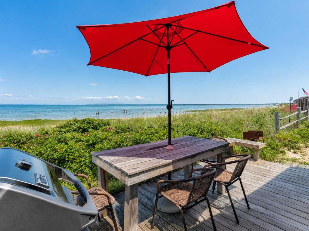 a picnic table with a red umbrella on the beach at Beachfront on Skaket Water Views in Orleans
