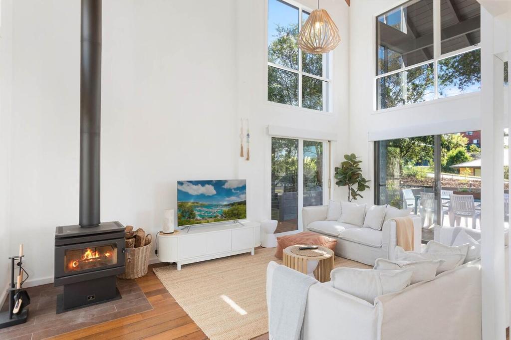 a living room with white furniture and a fireplace at Maisie's in Tathra