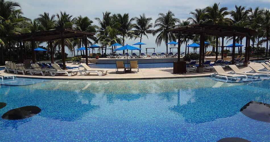 a large swimming pool with chairs and blue umbrellas at Villa 24C Los Cabos Monterrico in Monterrico
