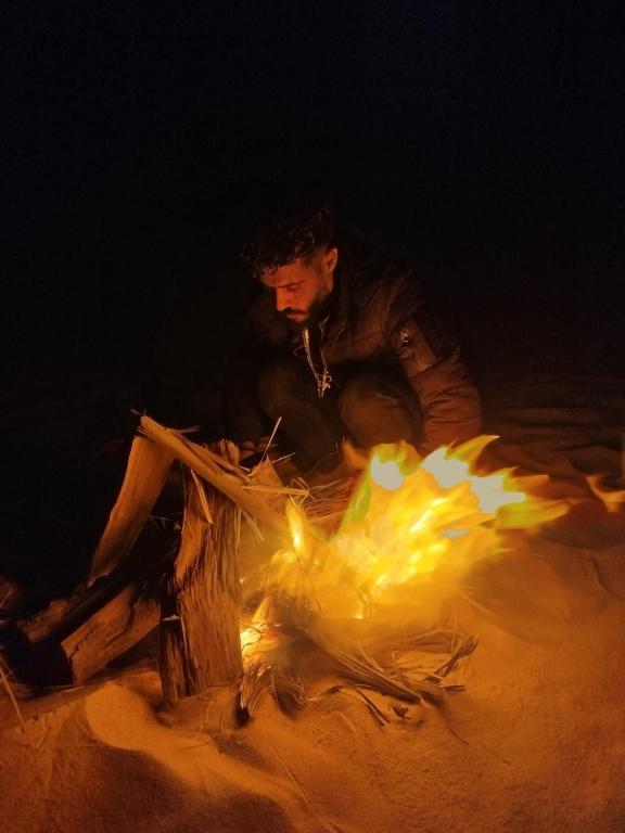 a man sitting next to a fire at night at مخيم همسات الصحراء in Siwa
