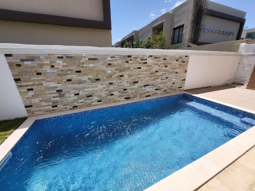 a swimming pool in front of a house with a brick wall at Luxuary pool appartement in La Marsa