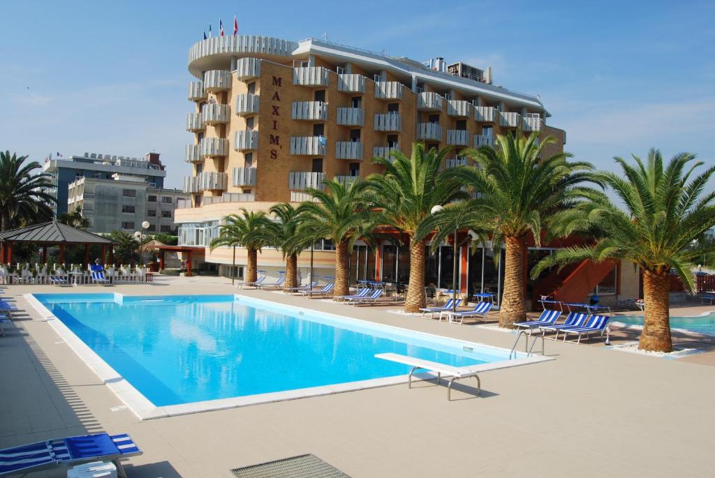 a swimming pool with palm trees and a hotel at Hotel Maxim's in Martinsicuro