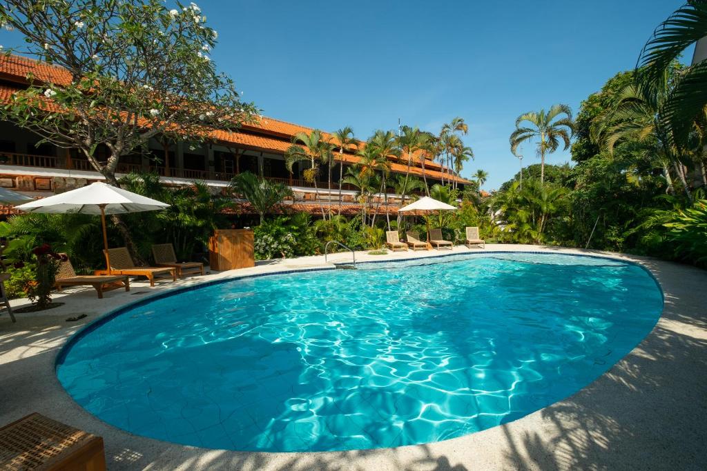 a pool with chairs and umbrellas next to a hotel at Uns Hotel - Bali in Legian