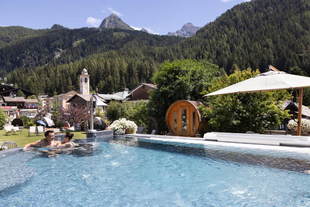 two people in a swimming pool with mountains in the background at Hotel Relais Des Glaciers - Adults Only in Champoluc