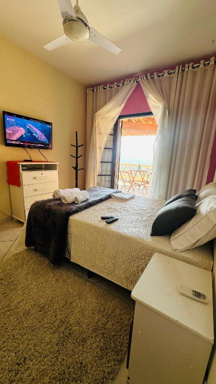a bedroom with a bed and a tv and a window at Suíte privativa - Centro Guararema in Guararema