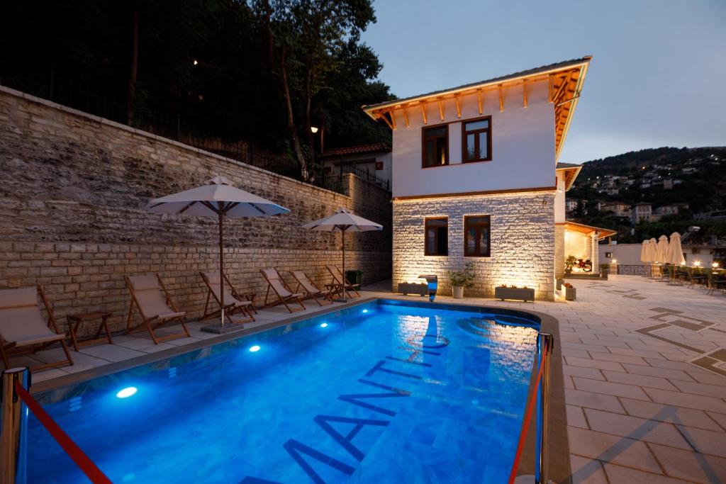 a swimming pool with chairs and umbrellas next to a building at Vila Mantho in Gjirokastër