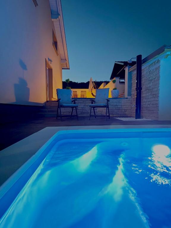 a swimming pool with two chairs next to a house at Holiday house Leona in Otočac