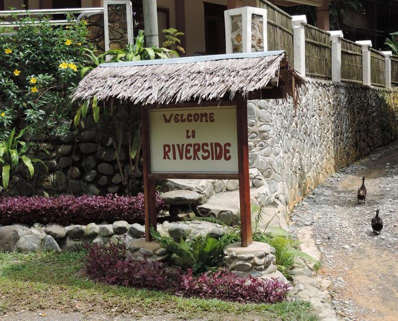 a sign in front of a stone building with chickens behind it at Riverside Guesthouse in Bukit Lawang