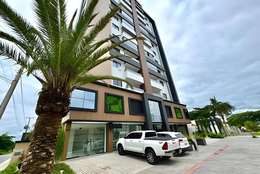 a white car parked in front of a building with a palm tree at Harmonie apto requintado | Centro | 200m do mar in Itapoa
