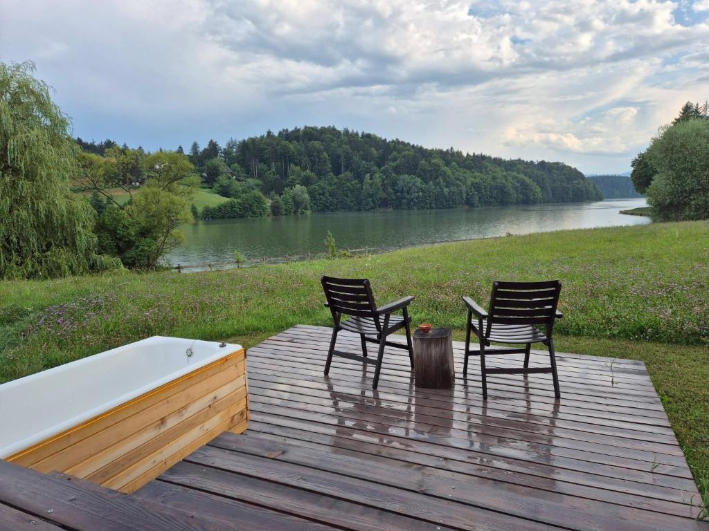 two chairs and a tub on a wooden deck with a lake at Lake window in Škofja Vas