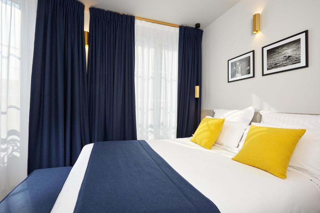 1 dormitorio con 1 cama con cortinas azules y almohadas amarillas en Hôtel Edouard 6 by Malone, en París