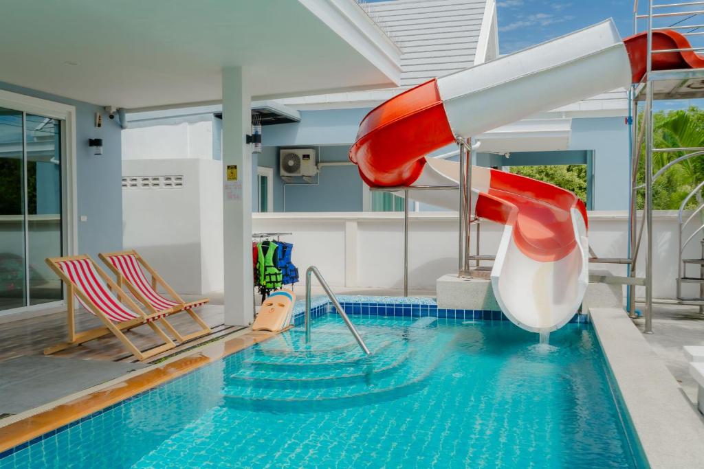 a water slide in a swimming pool with two chairs at พลอยพูลวิลล่า ชะอำ 2 Poolvilla Cha-am 2 in Cha Am