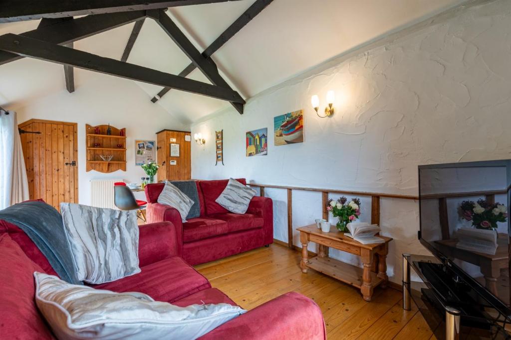 a living room with a red couch and a tv at Braddon - Treworgie Barton Cottages in Bude