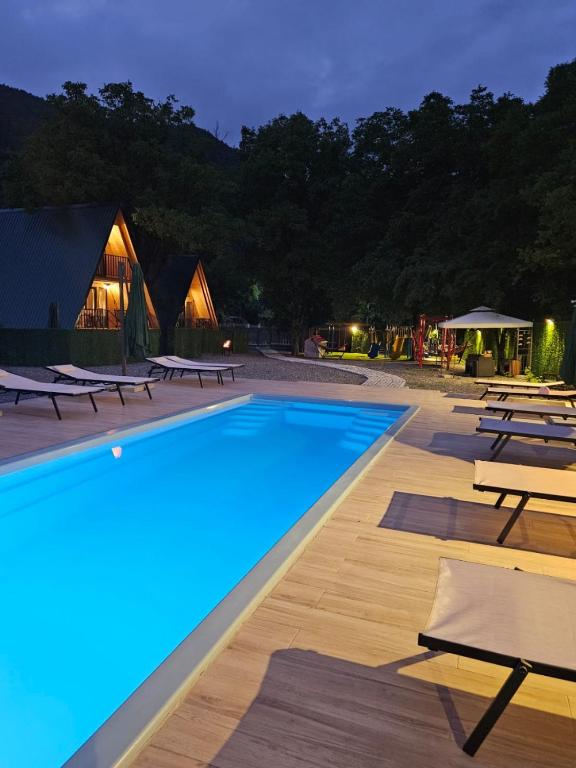 a swimming pool with tables and chairs at night at Riverside Ghari Cottages in Oni