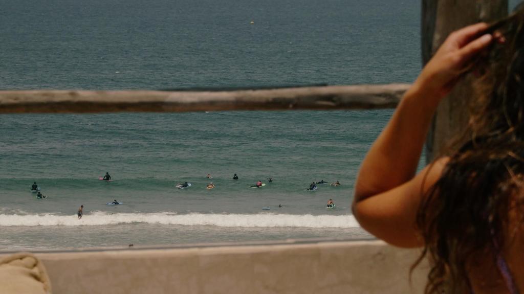 a woman looking out a window at people in the ocean at hyle Surfhouse in Agadir