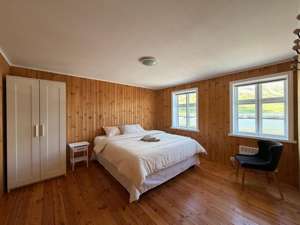 a bedroom with a bed and a chair and two windows at Cozy Home with Breathtaking Mountains and Sea Views in Flateyri