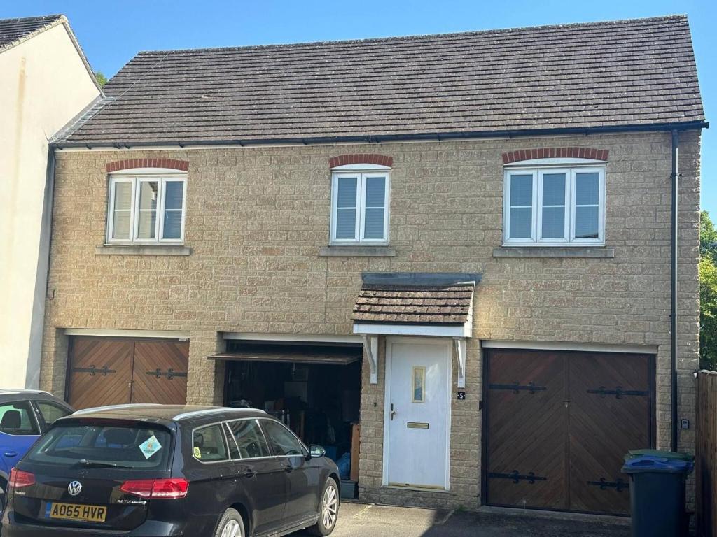 a house with two garage doors and a car parked in front at Super comfy, convenient two bedroom apartment in Corsham