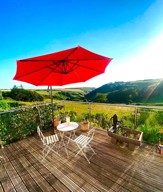 a table and chairs with a red umbrella on a deck at Strand Retreat in Tintagel