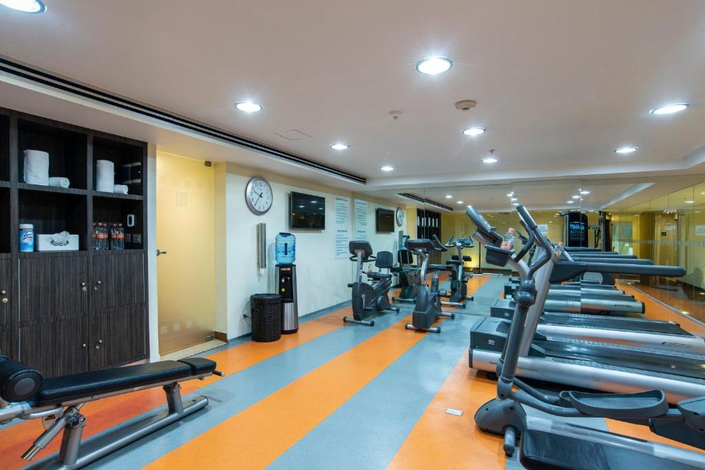 A long, brightly lit gym with cardio machines and a small bench area.