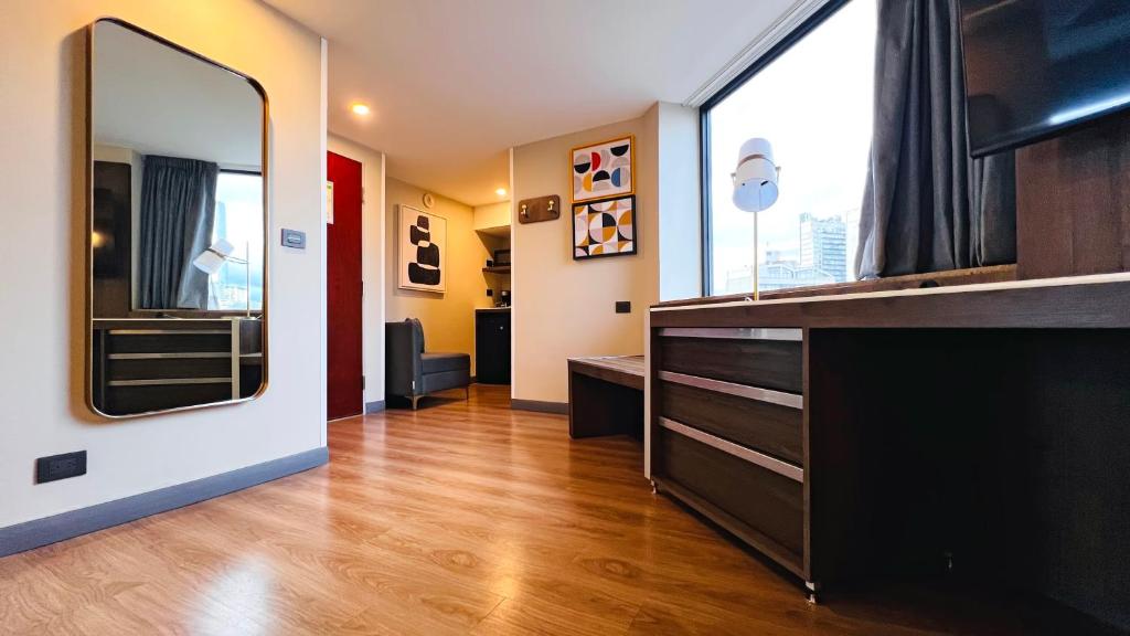 A wood-floored room entry and living area with dresser storage, mirror, artwork, and a city-facing window.